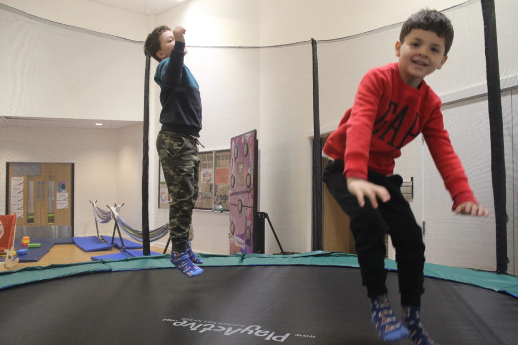 Two boys, one in red and one in blue are jumping on a large trampoline.