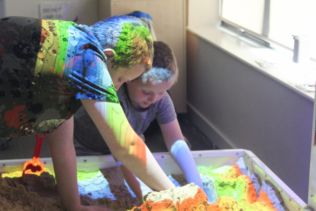 Two young boys are playing with a light up sandpit