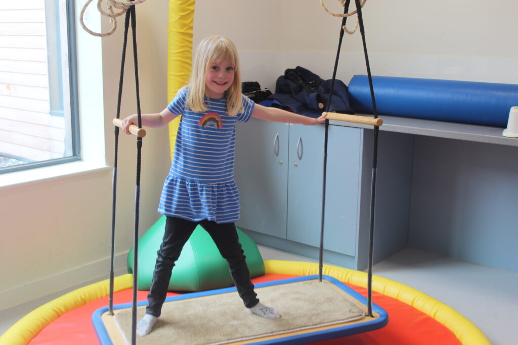 A girl is a blue dress is balancing on a platform swing