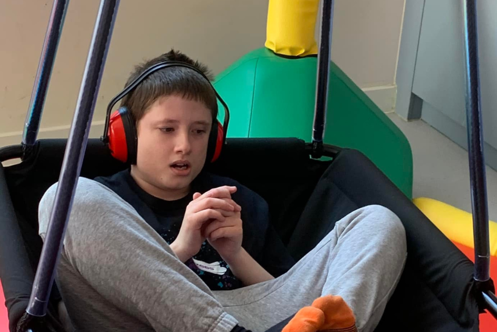 A child wearing noise cancelling headphones is sat in a platform swing