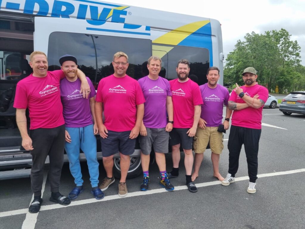 A group of men in pink and purple Gympanzees tops stood next to a bus