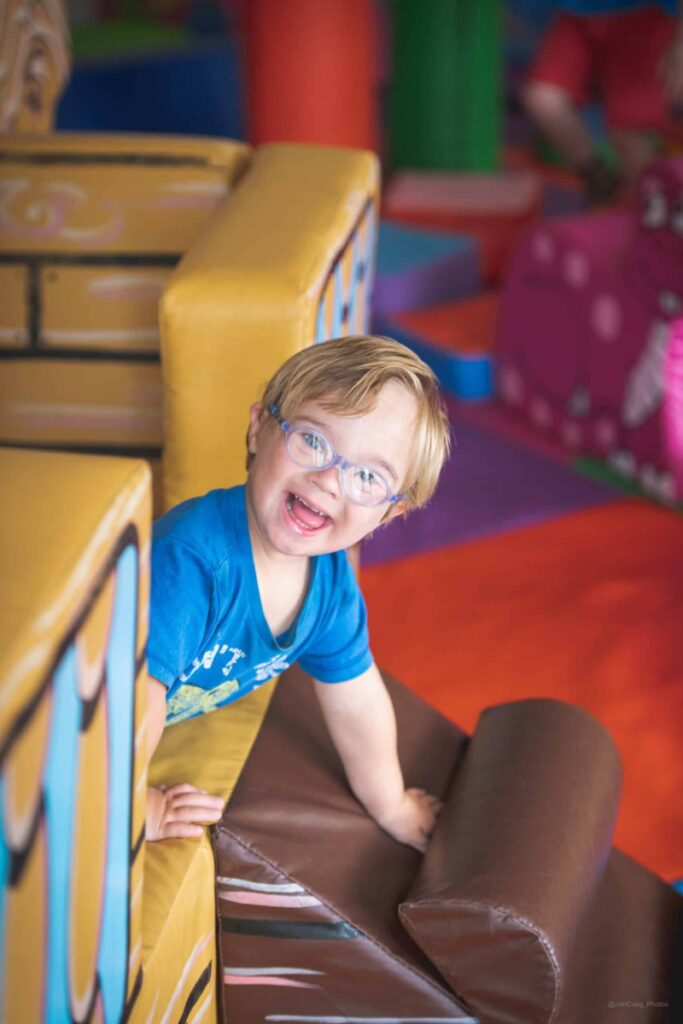 A small child with blonde hair is playing in a soft play pirate ship