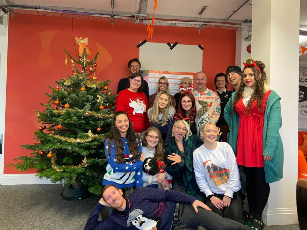 A group of people in an orange office stood in Christmas Jumpers