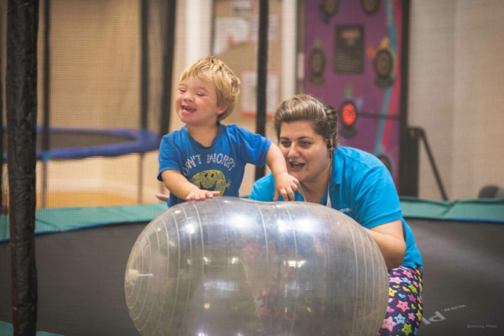 A young child and adult playing with a large see through sphere on a trampoline