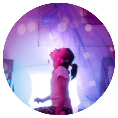 A young child in a dark sensory room with lights and colourful cloths