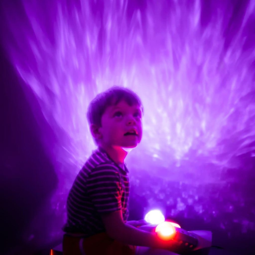 A small child is sat in a dark sensory room with purple lights.